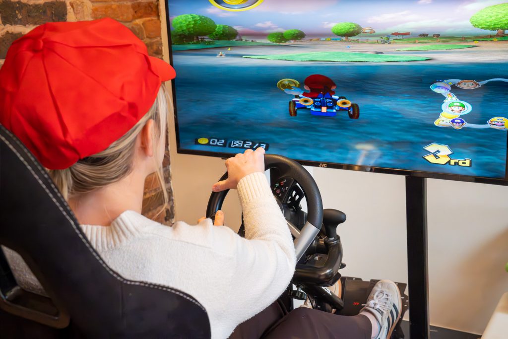 A person wearing a red hat and playing mario kart with hands on a steering wheel.