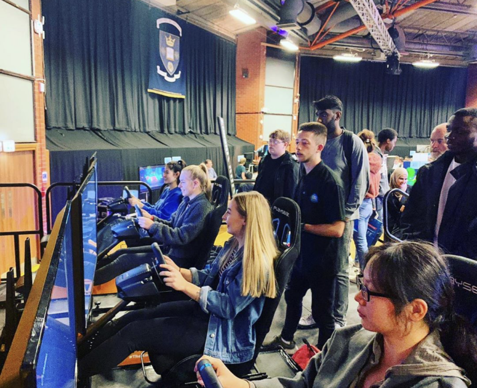 Four people playing a race car simulator at a busy event with a crowd of people watching.