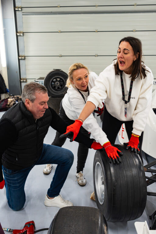 Three people changing a tire at a pit stop simulator.