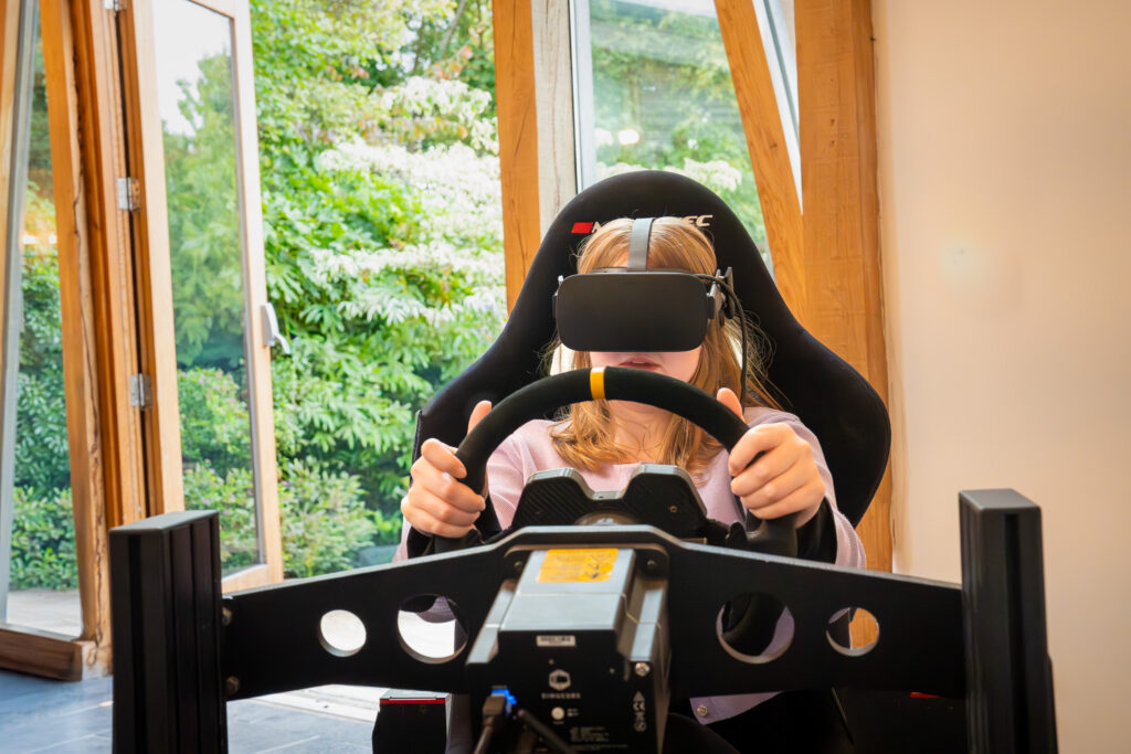 A woman wearing VR goggles sitting in a VR racing simulator with her hands on the steering wheel.