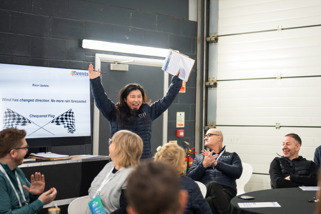 A woman standing in front a group of people with her hands in the air cheering.